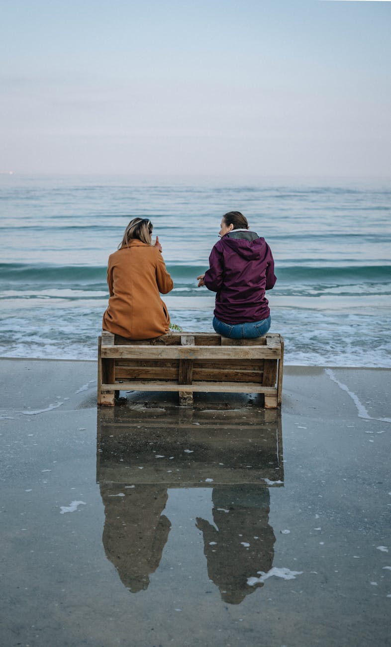 two people sitting on pallet on beach and talking